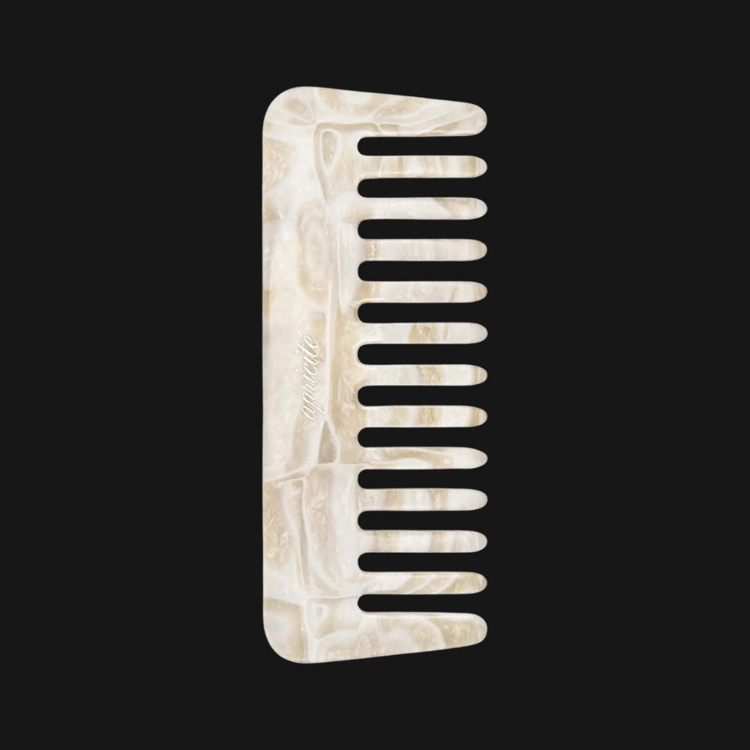 Ivory and beige pearlescent comb with a gold stamped logo on a black background